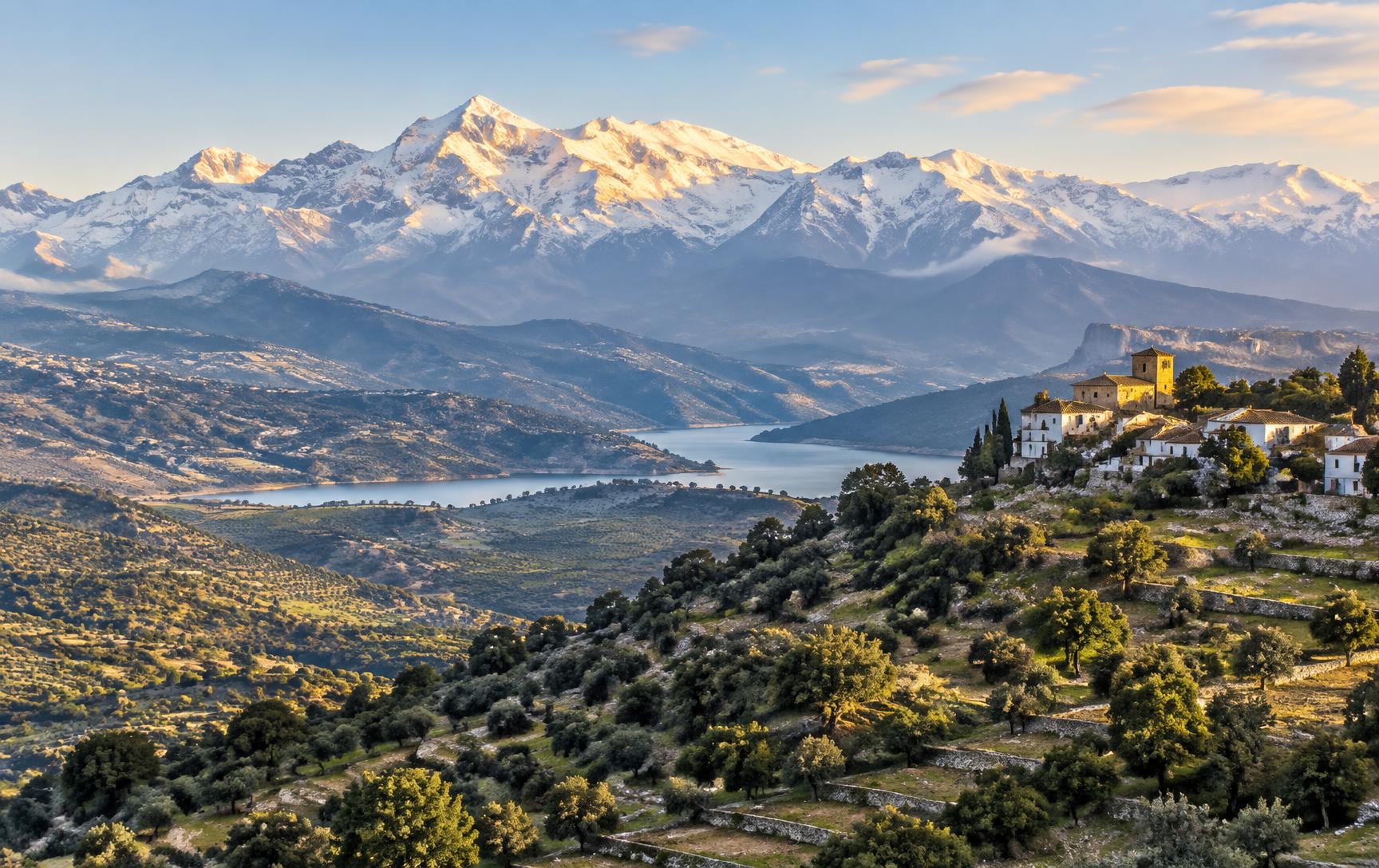 Snow-capped mountains rising above a green valley of oak groves